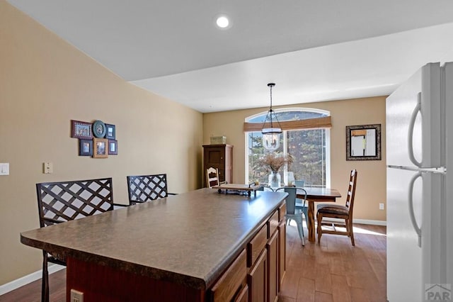 kitchen featuring baseboards, wood finished floors, freestanding refrigerator, and dark countertops