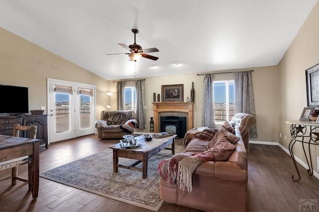living area with lofted ceiling, a ceiling fan, baseboards, a tiled fireplace, and hardwood / wood-style flooring
