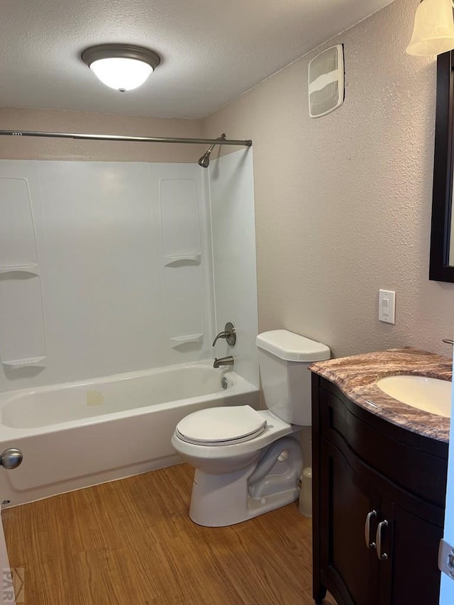 bathroom with wood finished floors, toilet, shower / tub combination, vanity, and a textured ceiling