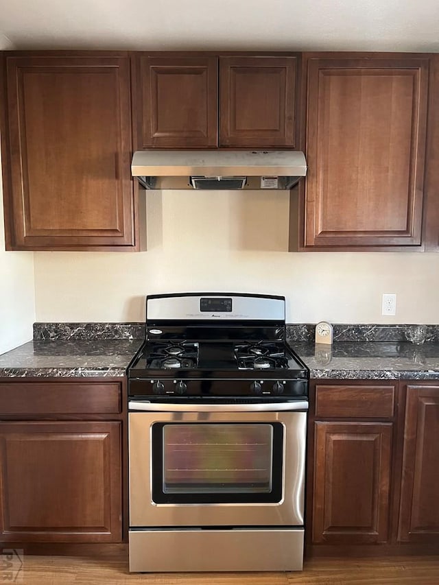 kitchen featuring stainless steel gas range, under cabinet range hood, light wood finished floors, and dark stone counters