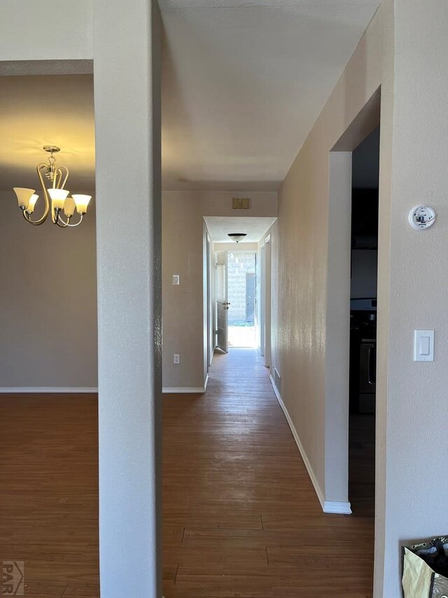 hallway featuring a chandelier, baseboards, and wood finished floors