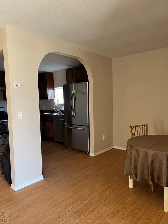 dining space featuring baseboards, light wood finished floors, and arched walkways