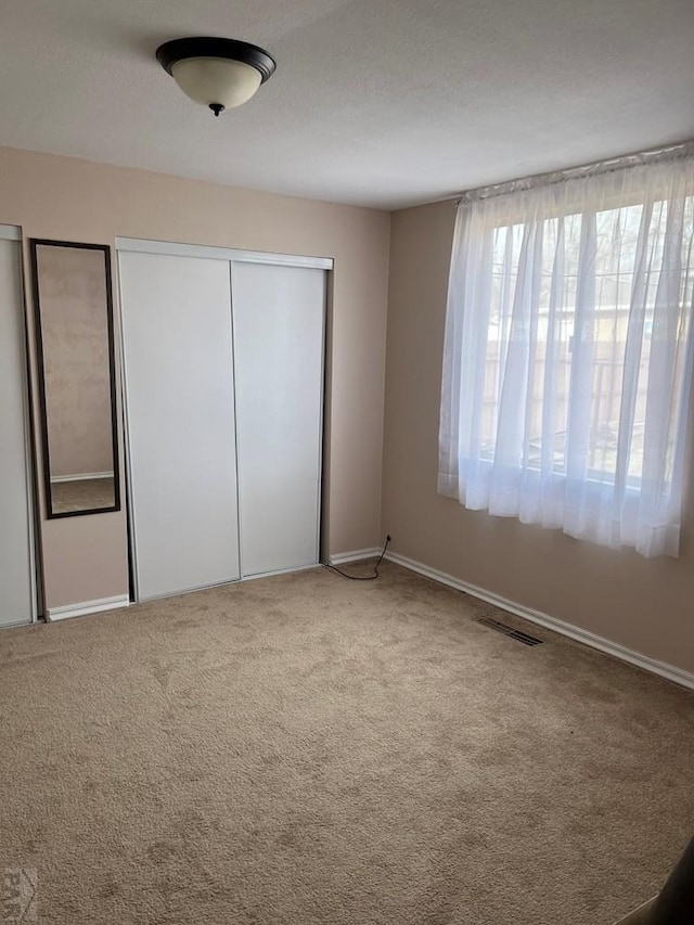 unfurnished bedroom with carpet floors, visible vents, a closet, and baseboards