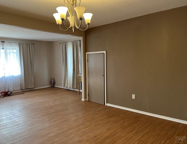 empty room featuring an inviting chandelier, light wood-style flooring, and baseboards