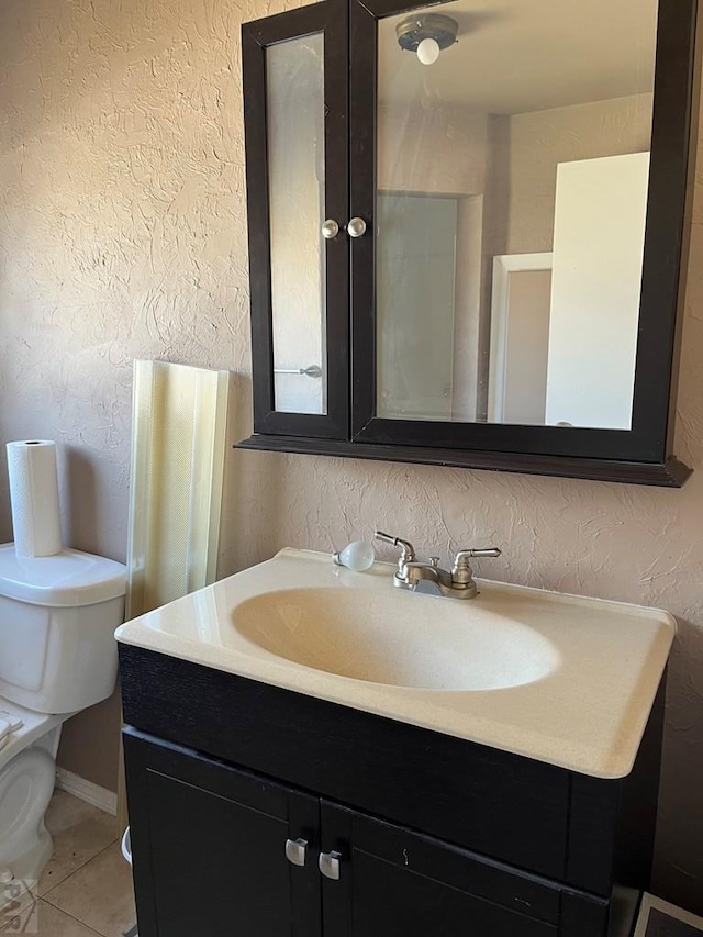 bathroom featuring tile patterned floors, toilet, a textured wall, and vanity
