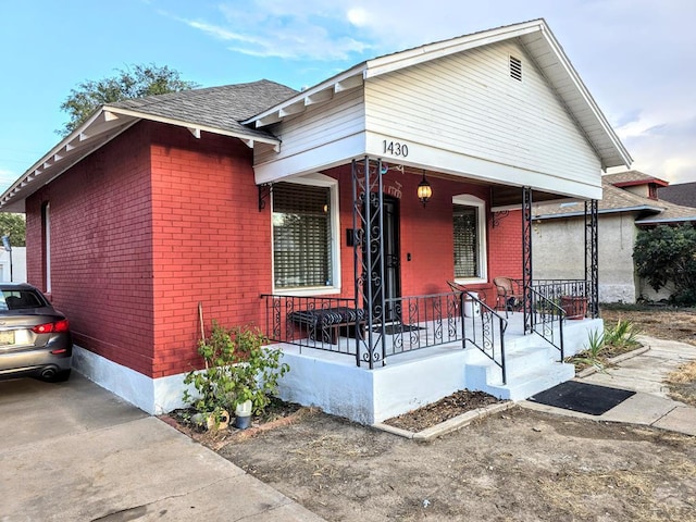 view of front facade featuring covered porch, roof with shingles, and brick siding