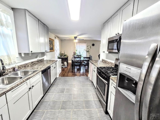 kitchen featuring stainless steel appliances, a ceiling fan, white cabinets, a sink, and dark stone countertops