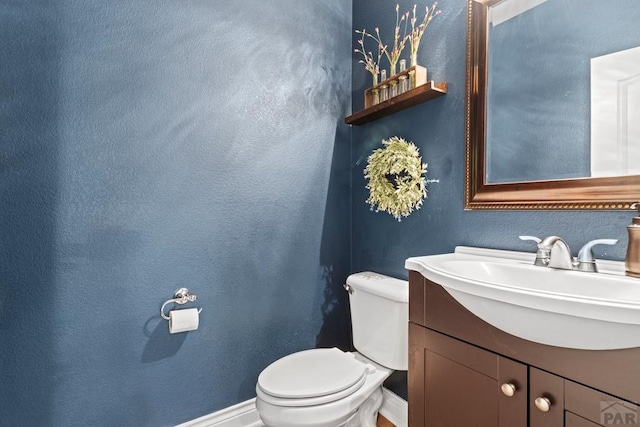 half bathroom with toilet, a textured wall, baseboards, and vanity