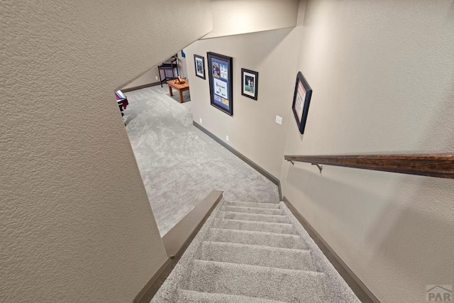 stairway with carpet, a textured wall, and baseboards