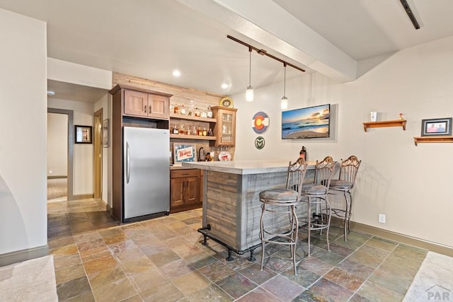 bar featuring baseboards, wet bar, stainless steel fridge, stone tile flooring, and pendant lighting