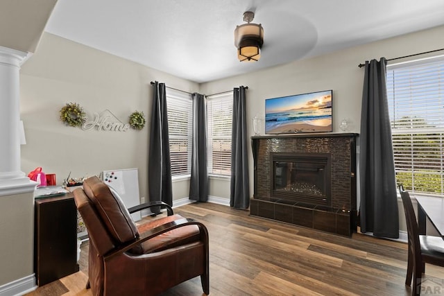 living area with decorative columns, a fireplace, baseboards, and wood finished floors