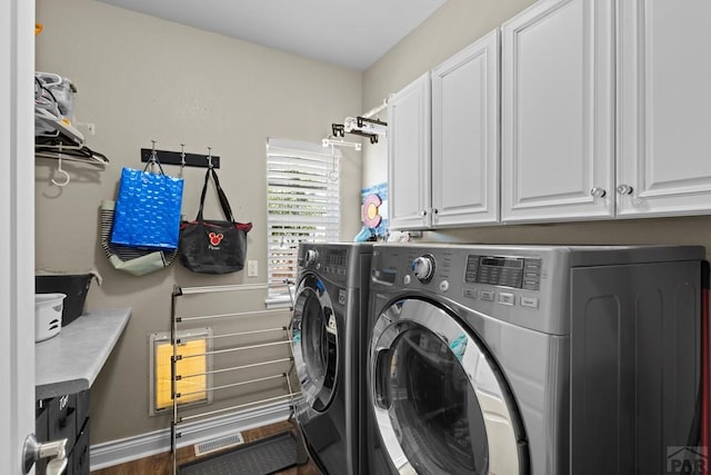 clothes washing area with washer and dryer, cabinet space, visible vents, and baseboards