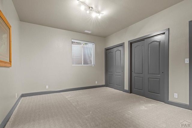 unfurnished bedroom featuring carpet, baseboards, and multiple closets