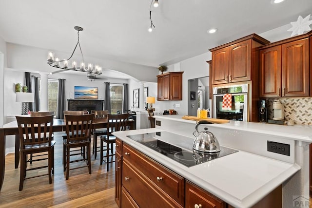 kitchen featuring decorative columns, black electric cooktop, light countertops, stainless steel oven, and pendant lighting