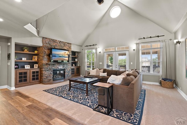 living area with baseboards, built in features, french doors, a stone fireplace, and light wood-style floors