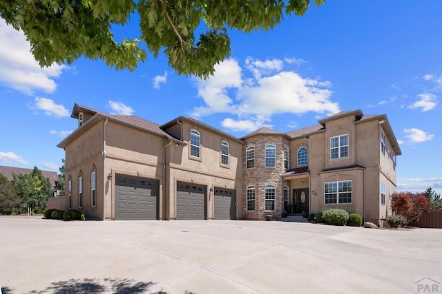 view of front of property featuring driveway, stone siding, an attached garage, and stucco siding