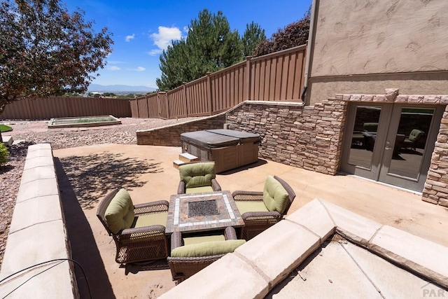 view of patio with french doors, a hot tub, an outdoor fire pit, a mountain view, and a fenced backyard