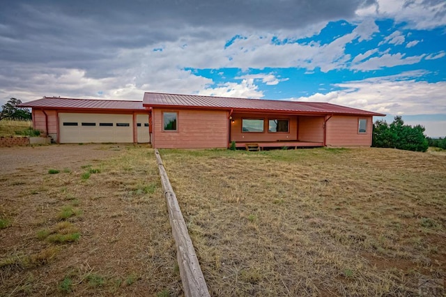 ranch-style home featuring a front lawn, metal roof, dirt driveway, and an attached garage
