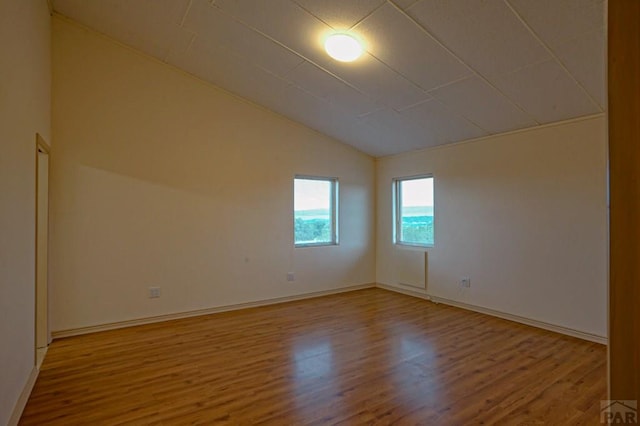 spare room with vaulted ceiling, wood finished floors, and baseboards