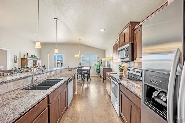 kitchen with brown cabinetry, lofted ceiling, appliances with stainless steel finishes, light wood-type flooring, and a sink