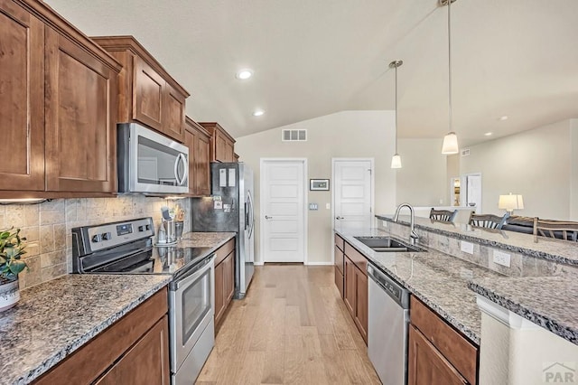 kitchen with stone countertops, stainless steel appliances, a sink, visible vents, and light wood-type flooring