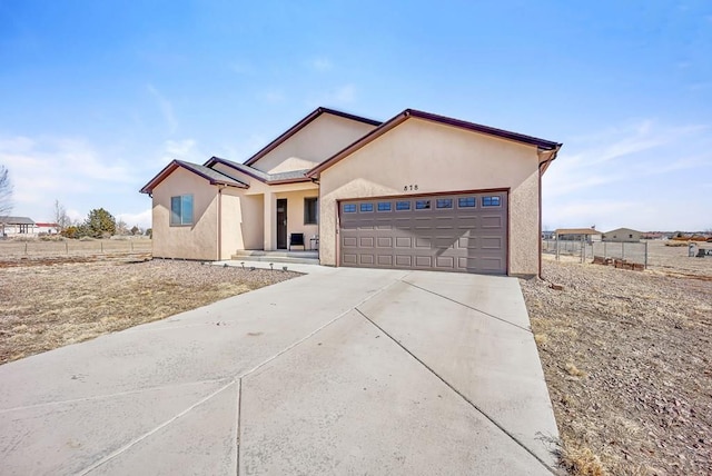 ranch-style house featuring driveway, fence, an attached garage, and stucco siding