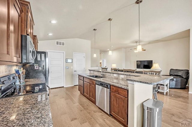 kitchen with lofted ceiling, stainless steel appliances, a sink, open floor plan, and dark stone countertops