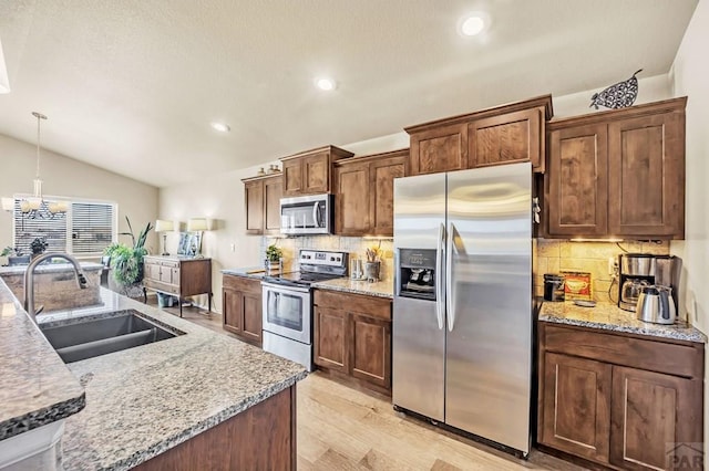 kitchen featuring lofted ceiling, light wood-style flooring, stainless steel appliances, pendant lighting, and a sink