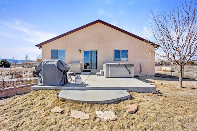 rear view of property with a hot tub, a patio, and stucco siding