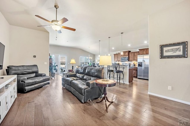 living area featuring lofted ceiling, light wood-style flooring, baseboards, and ceiling fan with notable chandelier