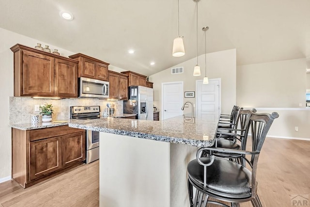 kitchen featuring appliances with stainless steel finishes, a kitchen bar, visible vents, and decorative backsplash