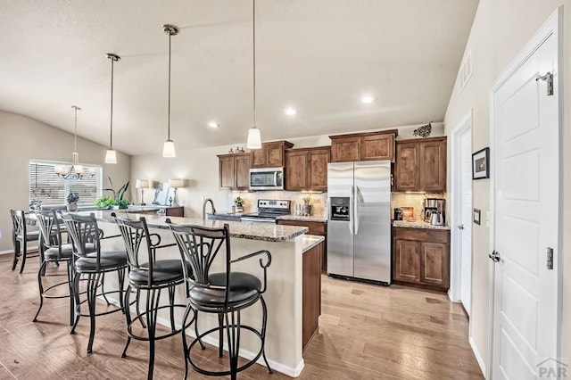 kitchen featuring a breakfast bar area, light wood-style flooring, a kitchen island with sink, appliances with stainless steel finishes, and tasteful backsplash