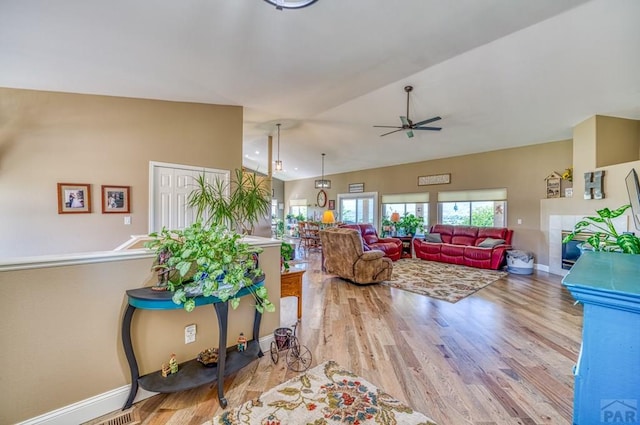 living room featuring vaulted ceiling, ceiling fan, light wood-style flooring, and baseboards