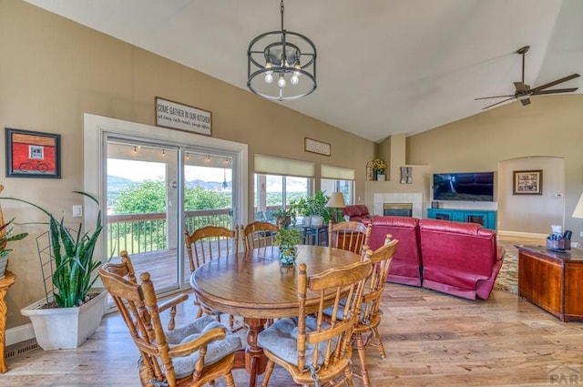 dining area with light wood finished floors, a fireplace, baseboards, and vaulted ceiling