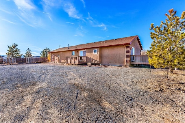 rear view of house featuring stucco siding, a wooden deck, and fence