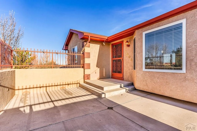 doorway to property with a patio, fence, and stucco siding