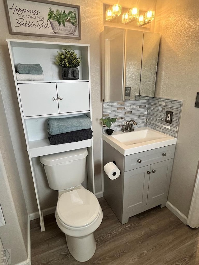 half bathroom with toilet, wood finished floors, vanity, baseboards, and tasteful backsplash