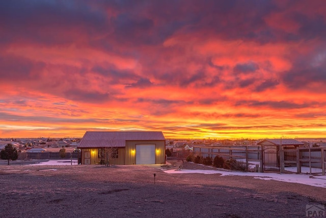 outdoor structure at dusk featuring an outbuilding, a residential view, fence, and a gate