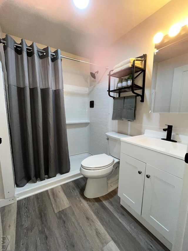 bathroom with toilet, a shower stall, wood finished floors, and vanity