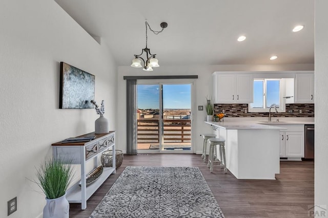 kitchen featuring a breakfast bar, pendant lighting, light countertops, white cabinets, and a sink