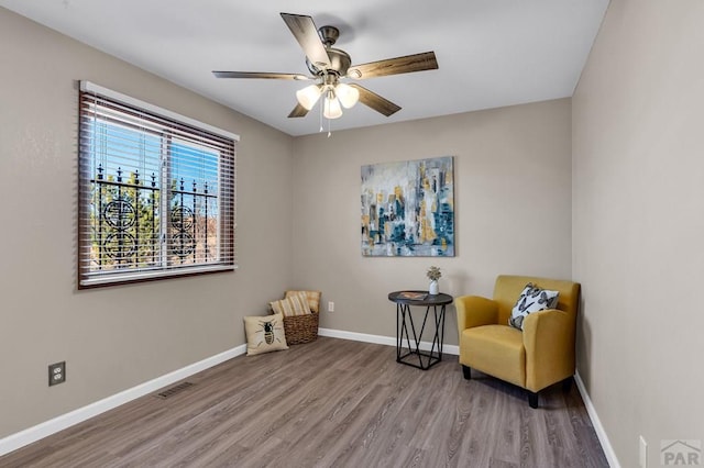 living area featuring baseboards, visible vents, ceiling fan, and wood finished floors