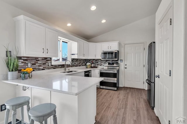 kitchen featuring stainless steel appliances, light countertops, white cabinetry, a sink, and a peninsula