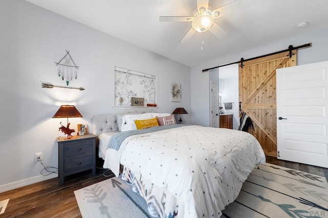 bedroom featuring a barn door, baseboards, dark wood finished floors, a ceiling fan, and connected bathroom