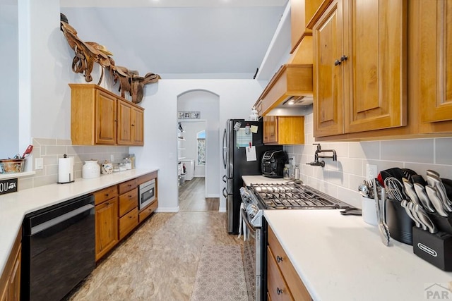 kitchen with arched walkways, brown cabinets, stainless steel appliances, light countertops, and backsplash