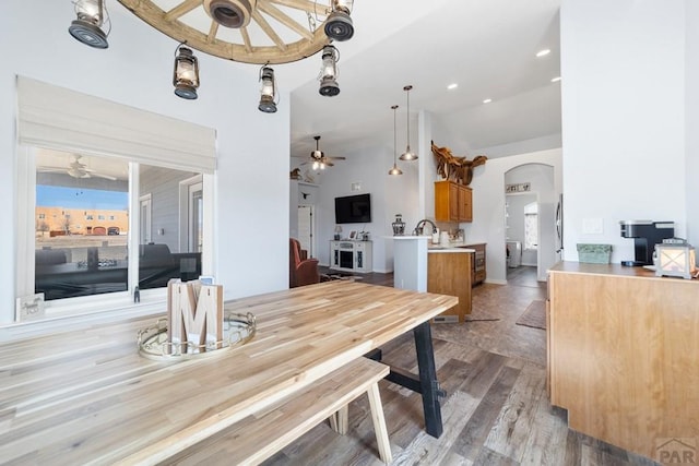 dining room with arched walkways, ceiling fan, vaulted ceiling, and light wood-style flooring