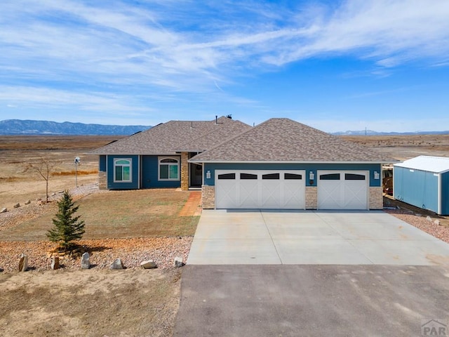 ranch-style home featuring a shingled roof, concrete driveway, an attached garage, a mountain view, and a front lawn