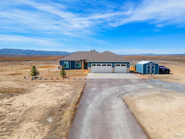 ranch-style home featuring driveway, a garage, an outbuilding, a storage unit, and a mountain view