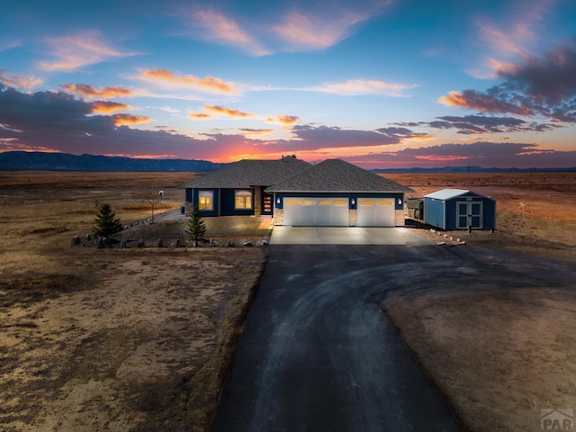 view of front of house with a storage unit, concrete driveway, an attached garage, a mountain view, and an outdoor structure