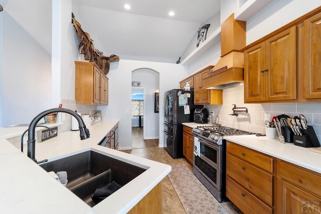 kitchen with range with two ovens, vaulted ceiling, light countertops, freestanding refrigerator, and brown cabinetry