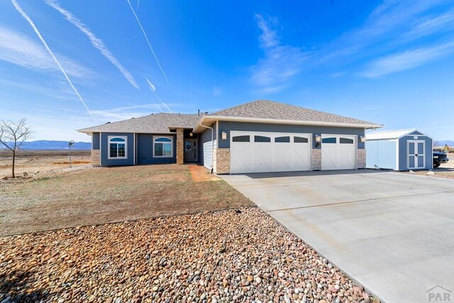 single story home featuring an outbuilding, a garage, a storage shed, a shingled roof, and driveway